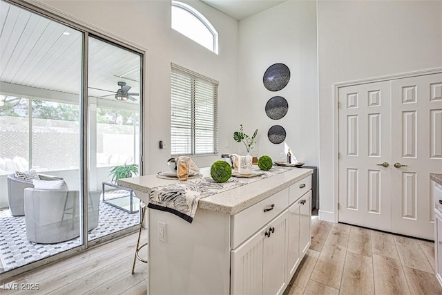 920 Siena Hills Ln, Las Vegas, NV 89144 - kitchen with light wood finished floors, white cabinets, a ceiling fan, a kitchen island, and a towering ceiling