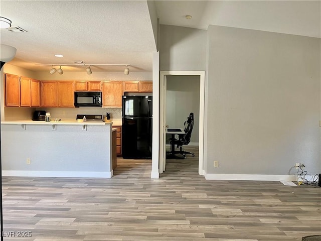 2627 S Durango Dr Unit 202, Las Vegas, NV 89117 - kitchen featuring black appliances, a peninsula, light wood finished floors, light countertops, and a kitchen bar