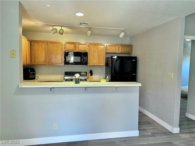 2627 S Durango Dr Unit 202, Las Vegas, NV 89117 - kitchen with black appliances, wood finished floors, a peninsula, light countertops, and brown cabinetry