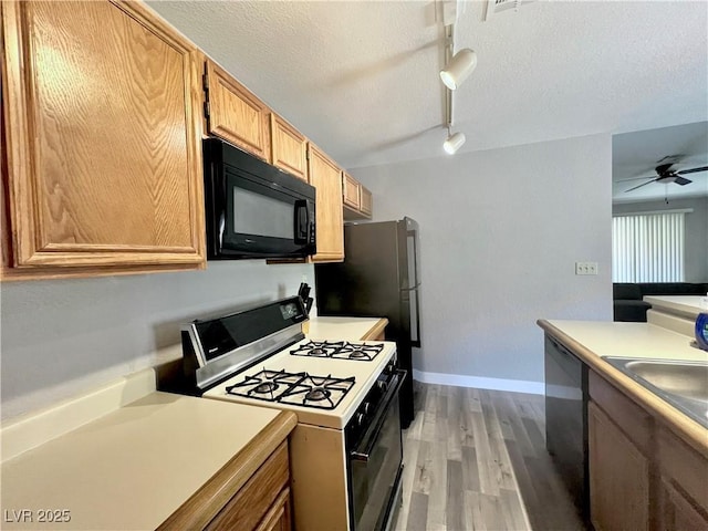 2627 S Durango Dr Unit 202, Las Vegas, NV 89117 - kitchen with white range with gas stovetop, black microwave, rail lighting, ceiling fan, and light wood-style floors