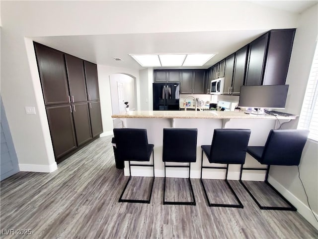 5104 Brookmere Dr, Las Vegas, NV 89130 - kitchen featuring black refrigerator, white microwave, a peninsula, light wood-style floors, and a breakfast bar area