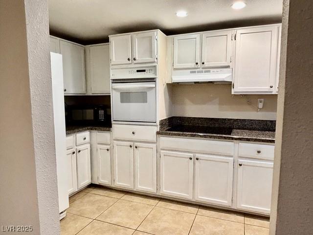 750 S Royal Crest Cir Unit 325, Las Vegas, NV 89169 - kitchen featuring black appliances, under cabinet range hood, white cabinets, light tile patterned floors, and dark stone counters