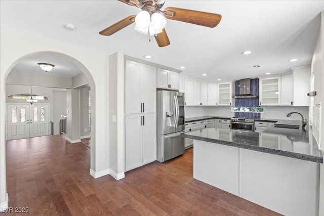 2842 Via Florentine St, Henderson, NV 89074 - kitchen featuring stainless steel appliances, wall chimney range hood, arched walkways, a ceiling fan, and dark wood finished floors