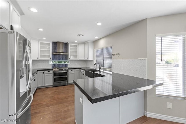 2842 Via Florentine St, Henderson, NV 89074 - kitchen featuring appliances with stainless steel finishes, wall chimney range hood, a peninsula, tasteful backsplash, and white cabinetry