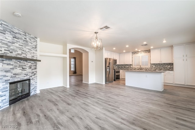 9578 Teton Vista Ave, Las Vegas, NV 89117 - unfurnished living room featuring arched walkways, light wood-style floors, a chandelier, a fireplace, and recessed lighting