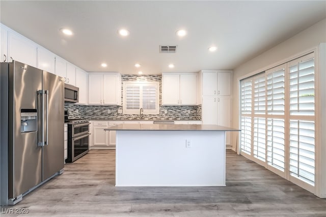 9578 Teton Vista Ave, Las Vegas, NV 89117 - kitchen featuring stainless steel appliances, a center island, white cabinetry, backsplash, and light wood-type flooring