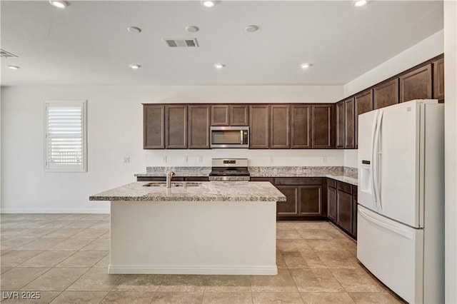 138 Red Sandstone Ave, North Las Vegas, NV 89031 - kitchen with appliances with stainless steel finishes, dark brown cabinetry, a kitchen island with sink, light stone counters, and light tile patterned floors