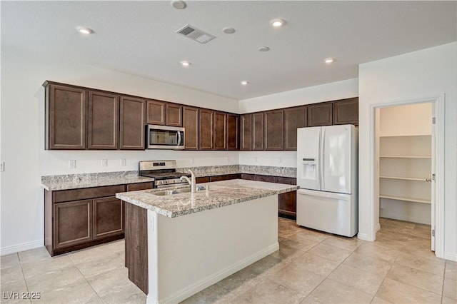 138 Red Sandstone Ave, North Las Vegas, NV 89031 - kitchen with appliances with stainless steel finishes, dark brown cabinetry, a center island with sink, light stone countertops, and light tile patterned floors