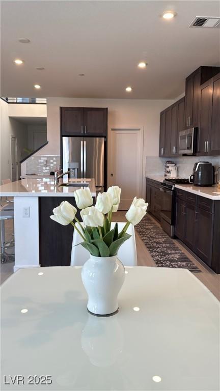3244 Timorasso Ave, Henderson, NV 89044 - kitchen featuring stainless steel appliances, dark brown cabinets, light countertops, decorative backsplash, and a kitchen breakfast bar