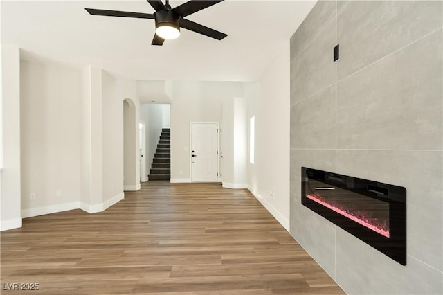 9349 Lakefront Color St, Las Vegas, NV 89178 - unfurnished living room with a ceiling fan, a fireplace, wood finished floors, stairway, and arched walkways