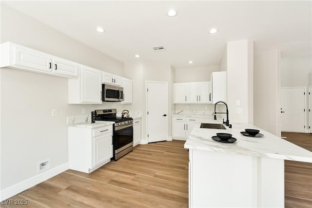 9349 Lakefront Color St, Las Vegas, NV 89178 - kitchen featuring appliances with stainless steel finishes, a peninsula, light wood-type flooring, light stone counters, and white cabinets