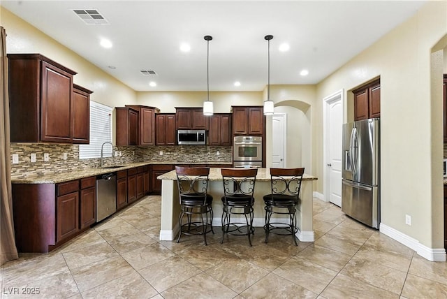 7330 Silent Water Way, Las Vegas, NV 89149 - kitchen featuring appliances with stainless steel finishes, arched walkways, a center island, backsplash, and light stone countertops