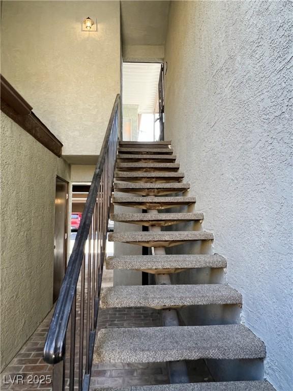 1420 Hialeah Dr Unit D, Las Vegas, NV 89119 - staircase featuring a textured wall and brick floors