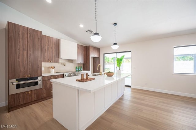 4594 Cabo Ln, Las Vegas, NV 89121 - kitchen featuring oven, light wood-style flooring, light countertops, tasteful backsplash, and a kitchen island with sink