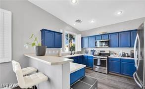 11018 Salernes St, Las Vegas, NV 89141 - kitchen featuring stainless steel appliances, a peninsula, lofted ceiling, blue cabinets, and a kitchen bar