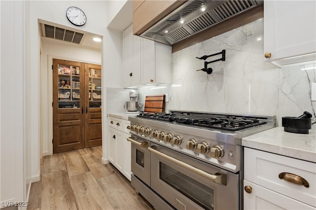 3227 Paintedhills Ave, Las Vegas, NV 89120 - kitchen with double oven range, custom exhaust hood, tasteful backsplash, white cabinetry, and light wood-style flooring