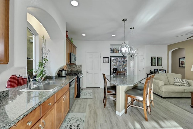 10167 Bishops Peak Ct, Las Vegas, NV 89141 - kitchen with appliances with stainless steel finishes, brown cabinetry, a kitchen bar, light wood finished floors, and arched walkways