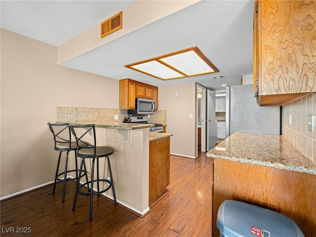 3740 Broadriver Dr, Las Vegas, NV 89108 - kitchen featuring appliances with stainless steel finishes, dark wood finished floors, backsplash, a peninsula, and brown cabinets