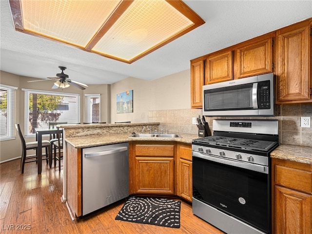 3740 Broadriver Dr, Las Vegas, NV 89108 - kitchen with appliances with stainless steel finishes, a peninsula, brown cabinets, and decorative backsplash