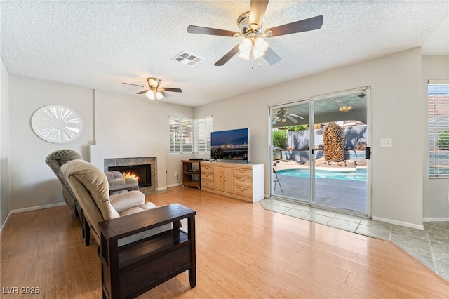 1337 Maplegrove Cir, Las Vegas, NV 89108 - living room with a tiled fireplace, a textured ceiling, ceiling fan, and light wood-style flooring