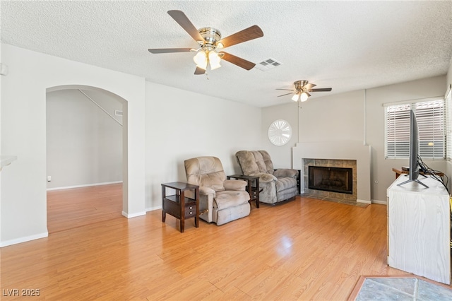 1337 Maplegrove Cir, Las Vegas, NV 89108 - living area with a tiled fireplace, a textured ceiling, ceiling fan, and light wood-type flooring