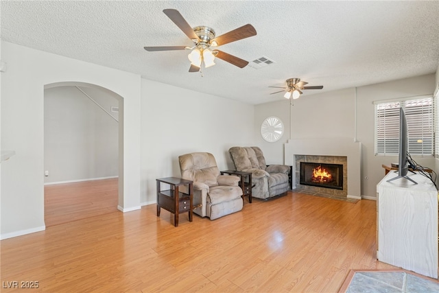 1337 Maplegrove Cir, Las Vegas, NV 89108 - living area with light wood finished floors, a tiled fireplace, a textured ceiling, arched walkways, and a ceiling fan