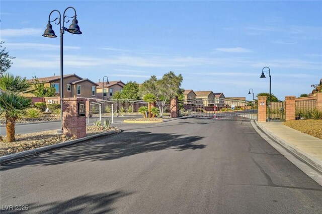 6373 Beavertail Pond Ave, Las Vegas, NV 89122 - view of asphalt road with a gate, street lights, a residential view, curbs, and sidewalks