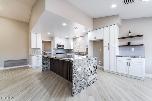 8904 Marble Dr, Las Vegas, NV 89134 - kitchen with stainless steel microwave, light wood-type flooring, light stone countertops, white cabinets, and recessed lighting