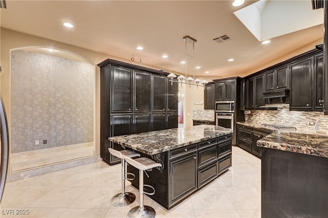 7751 Radcliff St, Las Vegas, NV 89123 - kitchen featuring stainless steel appliances, a kitchen island, dark stone countertops, arched walkways, and decorative backsplash
