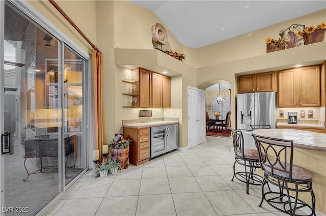 216 Chestnut Ridge Cir, Henderson, NV 89012 - kitchen with stainless steel fridge with ice dispenser, arched walkways, high vaulted ceiling, light countertops, and a kitchen bar