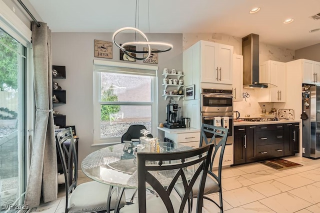 5021 Cliffrose Dr, Las Vegas, NV 89130 - kitchen featuring wall chimney range hood, stainless steel appliances, white cabinets, a chandelier, and plenty of natural light