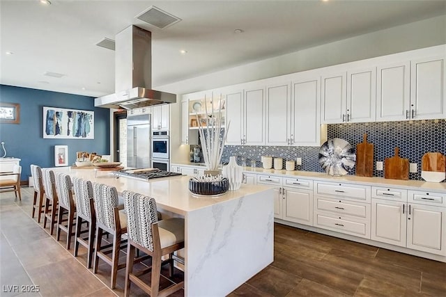 4152 Yucca Bloom St Unit 1, Las Vegas, NV 89135 - kitchen with island range hood, stainless steel appliances, white cabinetry, decorative backsplash, and a kitchen breakfast bar