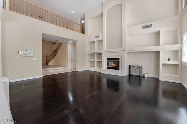 8901 Goldstone Ave, Las Vegas, NV 89143 - unfurnished living room with built in features, stairs, wood finished floors, a towering ceiling, and a glass covered fireplace