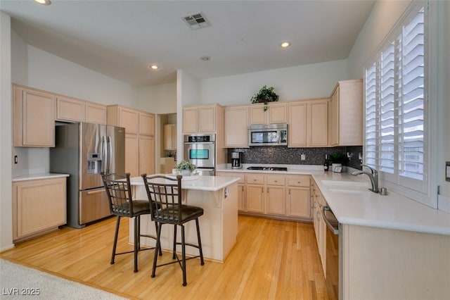 1414 Doggett Ave, Las Vegas, NV 89123 - kitchen with stainless steel appliances, light brown cabinets, a kitchen island, a kitchen bar, and light wood-style floors