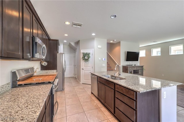 9237 S Chieftain St, Las Vegas, NV 89178 - kitchen featuring appliances with stainless steel finishes, a center island with sink, dark brown cabinetry, light stone countertops, and light tile patterned flooring