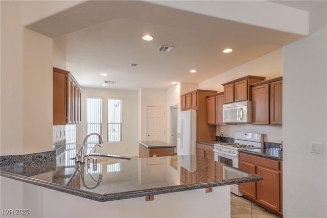 3813 Jasmine Heights Ave, North Las Vegas, NV 89081 - kitchen featuring white appliances, brown cabinets, a center island, dark stone counters, and recessed lighting