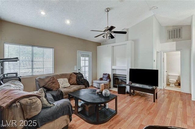 1600 N Torrey Pines Dr Unit 202, Las Vegas, NV 89108 - living area with a textured ceiling, a glass covered fireplace, vaulted ceiling, ceiling fan, and light wood-type flooring