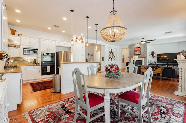 7209 Millerbird St, North Las Vegas, NV 89084 - dining area with a fireplace, a ceiling fan, light wood-type flooring, a chandelier, and recessed lighting