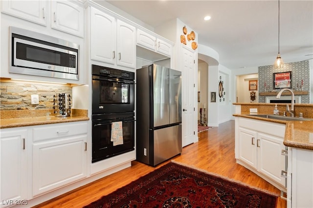 7209 Millerbird St, North Las Vegas, NV 89084 - kitchen featuring appliances with stainless steel finishes, light wood finished floors, decorative backsplash, arched walkways, and white cabinets