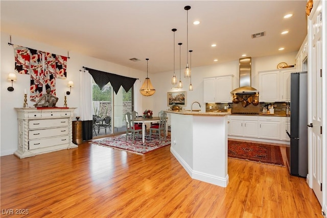 7209 Millerbird St, North Las Vegas, NV 89084 - kitchen with wall chimney range hood, black electric cooktop, white cabinets, light wood-type flooring, and freestanding refrigerator