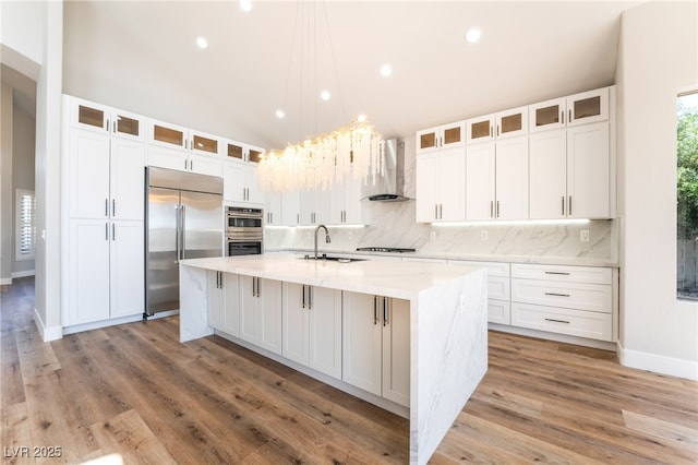 1016 Eaglewood Dr, Las Vegas, NV 89144 - kitchen with wall chimney range hood, appliances with stainless steel finishes, tasteful backsplash, a center island with sink, and white cabinetry