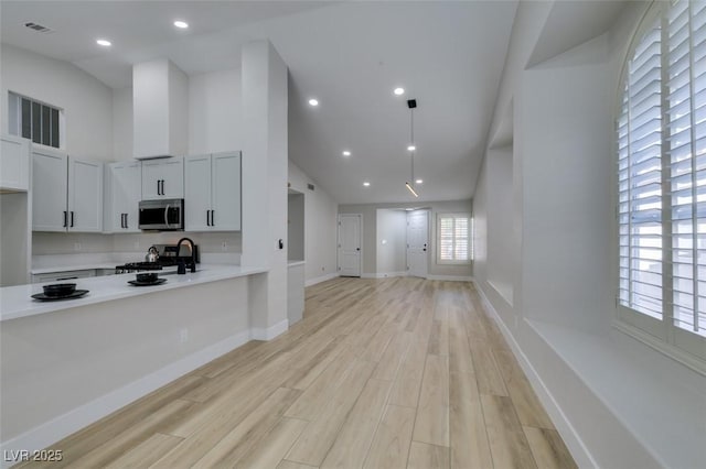 1844 Grand Prairie Ave, North Las Vegas, NV 89032 - kitchen with stainless steel microwave, light countertops, stove, light wood finished floors, and high vaulted ceiling