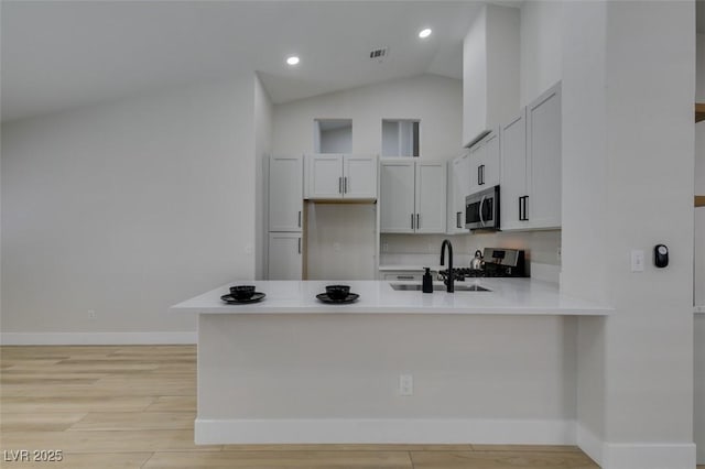 1844 Grand Prairie Ave, North Las Vegas, NV 89032 - kitchen with stainless steel appliances, a peninsula, lofted ceiling, light countertops, and light wood-style flooring