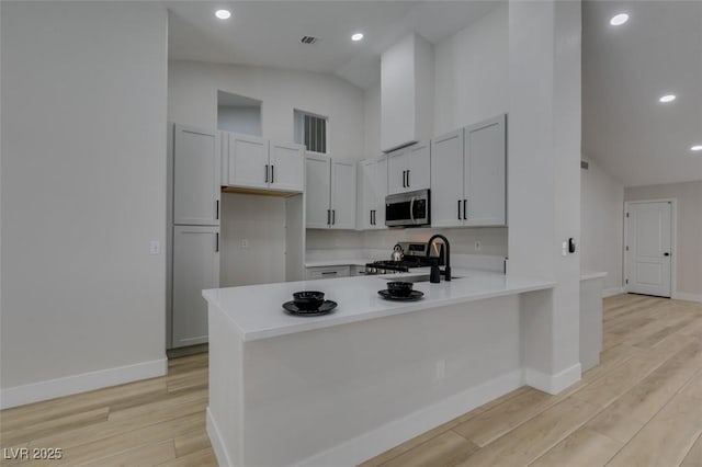 1844 Grand Prairie Ave, North Las Vegas, NV 89032 - kitchen featuring stainless steel microwave, a peninsula, light wood-style flooring, light countertops, and high vaulted ceiling