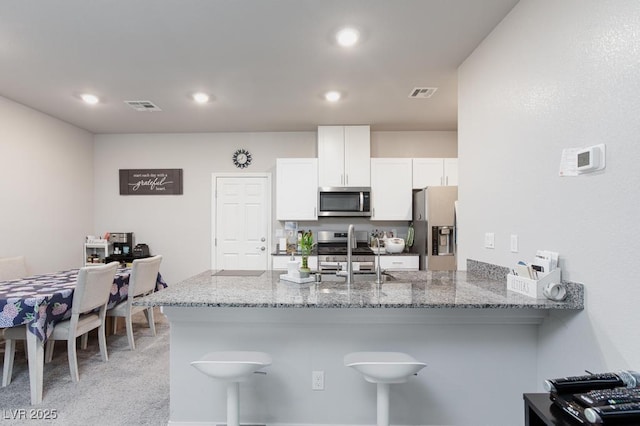 7212 Sunray Point St, North Las Vegas, NV 89084 - kitchen featuring stainless steel appliances, white cabinets, light stone counters, a breakfast bar area, and a peninsula