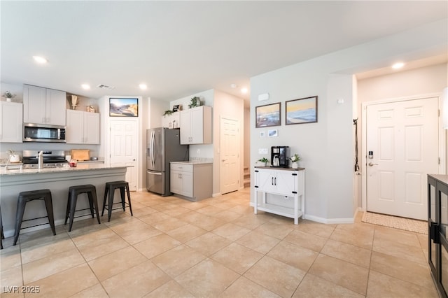 9237 Brayden Bay St, Las Vegas, NV 89178 - kitchen featuring appliances with stainless steel finishes, light tile patterned floors, a breakfast bar, recessed lighting, and light stone countertops