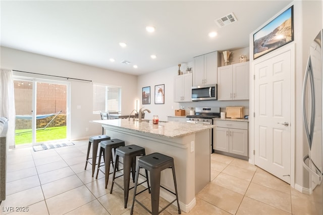 9237 Brayden Bay St, Las Vegas, NV 89178 - kitchen with appliances with stainless steel finishes, a center island with sink, a kitchen breakfast bar, light tile patterned flooring, and light stone counters