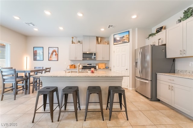 9237 Brayden Bay St, Las Vegas, NV 89178 - kitchen with appliances with stainless steel finishes, a kitchen breakfast bar, a center island with sink, light tile patterned flooring, and light stone countertops