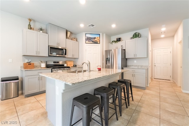 9237 Brayden Bay St, Las Vegas, NV 89178 - kitchen featuring appliances with stainless steel finishes, a breakfast bar area, light tile patterned flooring, a center island with sink, and light stone countertops