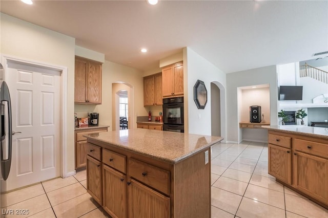 8929 Glenistar Gate Ave, Las Vegas, NV 89143 - kitchen with arched walkways, a center island, light tile patterned floors, light stone counters, and stainless steel refrigerator with ice dispenser
